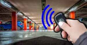 A person's hand holding a remote starter with bars going off it towards cars in a parking garage
