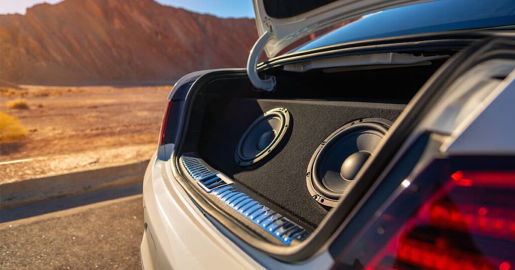 A vehicle in the desert with it's trunk open to reveal a subwoofer set
