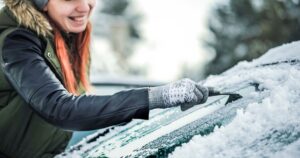 A woman with red hair scraping ice off a car windshield