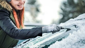 A woman with red hair scraping ice off a car windshield