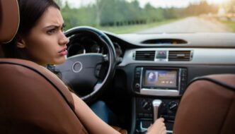 A confused looking young woman turning her head to look towards the rear of her vehicle as she sits in the driver seat